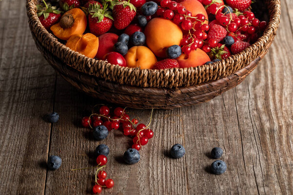 close up view of ripe seasonal berries and apricots in wicker basket on wooden table with copy space