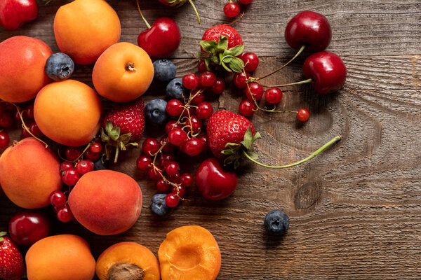 top view of ripe delicious fresh berries and apricots on wooden table