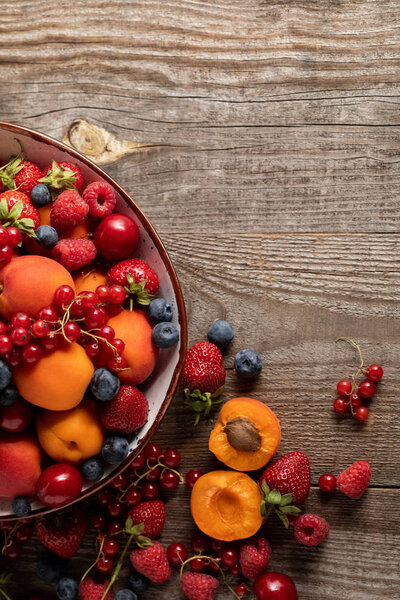 top view of ripe delicious berries and apricots in plate on wooden table with copy space