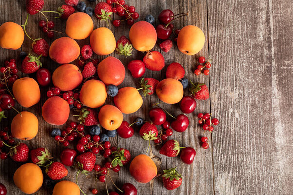 top view of ripe delicious seasonal berries scattered with fresh apricots on wooden table 