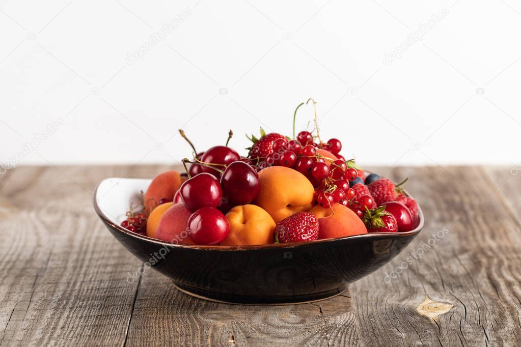 plate with mixed delicious ripe berries on wooden table isolated on white