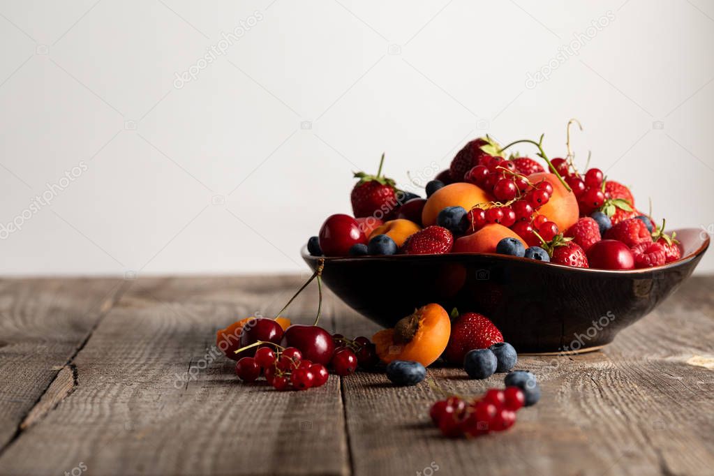 plate with fresh mixed delicious berries on wooden table isolated on white