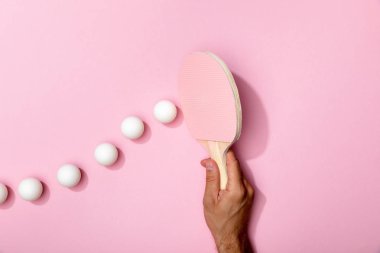 pembe arka plan üzerinde beyaz topları yakın masa tenisi raket tutan adam kırpılmış görünümü