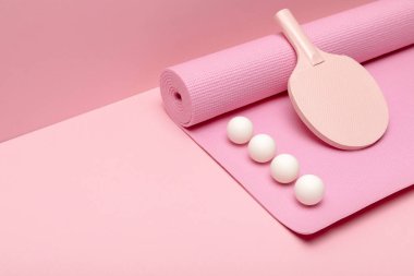 düz pembe arka plan üzerinde fitness mat üzerinde beyaz ping-pong topları ve raket ile yatıyordu