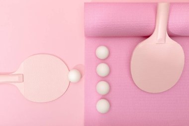 top view of white ping-pong balls and rackets on fitness mat on pink background
