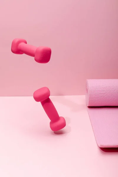 粉红色明亮的哑铃悬浮在空气中附近的橡胶健身垫在粉红色背景 — 图库照片