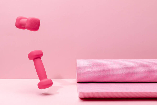 pink bright dumbbells levitating in air near fitness mat on pink background