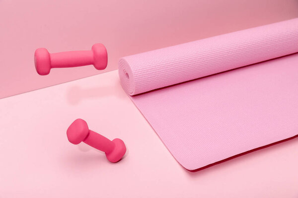 pink bright dumbbells levitating in air near rubber fitness mat on pink background