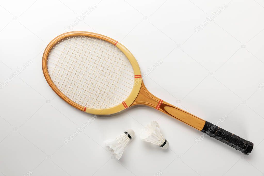 top view of white badminton shuttlecocks scattered near wooden racket on white background