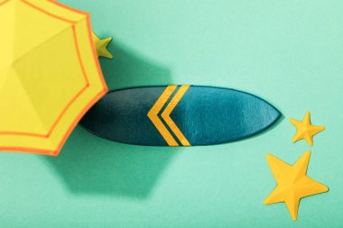 turkuaz arka plan üzerinde denizyıldızları ve sörf tahtası yakınında kağıt sarı şemsiye üst görünümü