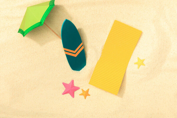 top view of paper umbrella, towel, starfishes and surfboard on sandy background