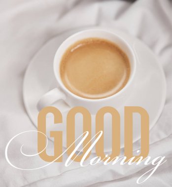 top view of coffee in white cup on saucer near silver alarm clock on bedding with good morning illustration  clipart