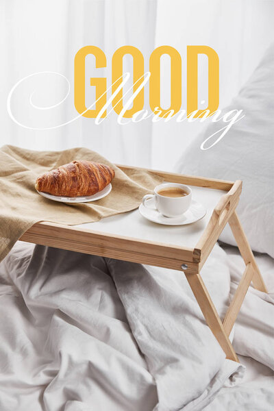 coffee and croissant served on wooden tray on white bed with pillow with good morning illustration