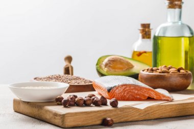 fresh salmon, nuts and avocado on wooden chopping board near oil isolated on grey, ketogenic diet menu clipart