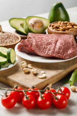 gri, ketojenik diyet menüsünde izole fındık ve sebze yakınında ahşap doğrama tahtası üzerinde çiğ et