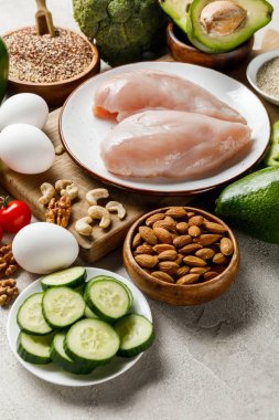 fresh raw chicken breasts on white plate near nuts, eggs and green vegetables, ketogenic diet menu clipart