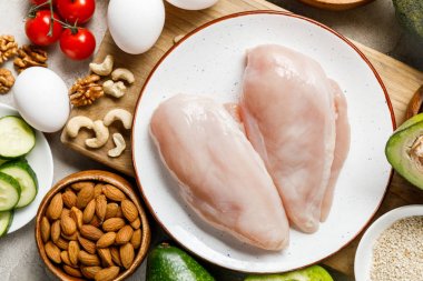 top view of fresh raw chicken breasts near nuts, eggs and vegetables, ketogenic diet menu clipart