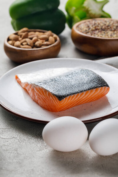 selective focus of fresh raw salmon on white plate near nuts and eggs, ketogenic diet menu