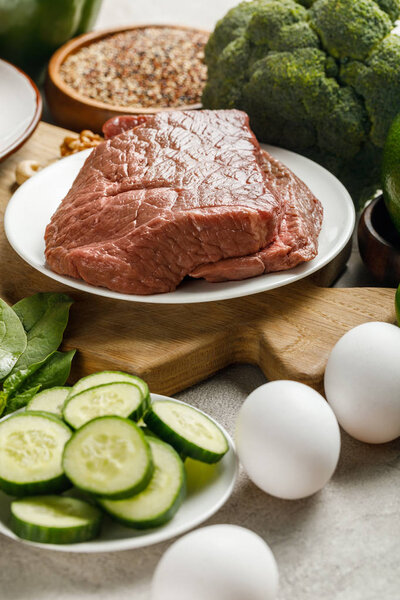 close up view of raw meat on wooden chopping board near eggs and cucumbers, , ketogenic diet menu