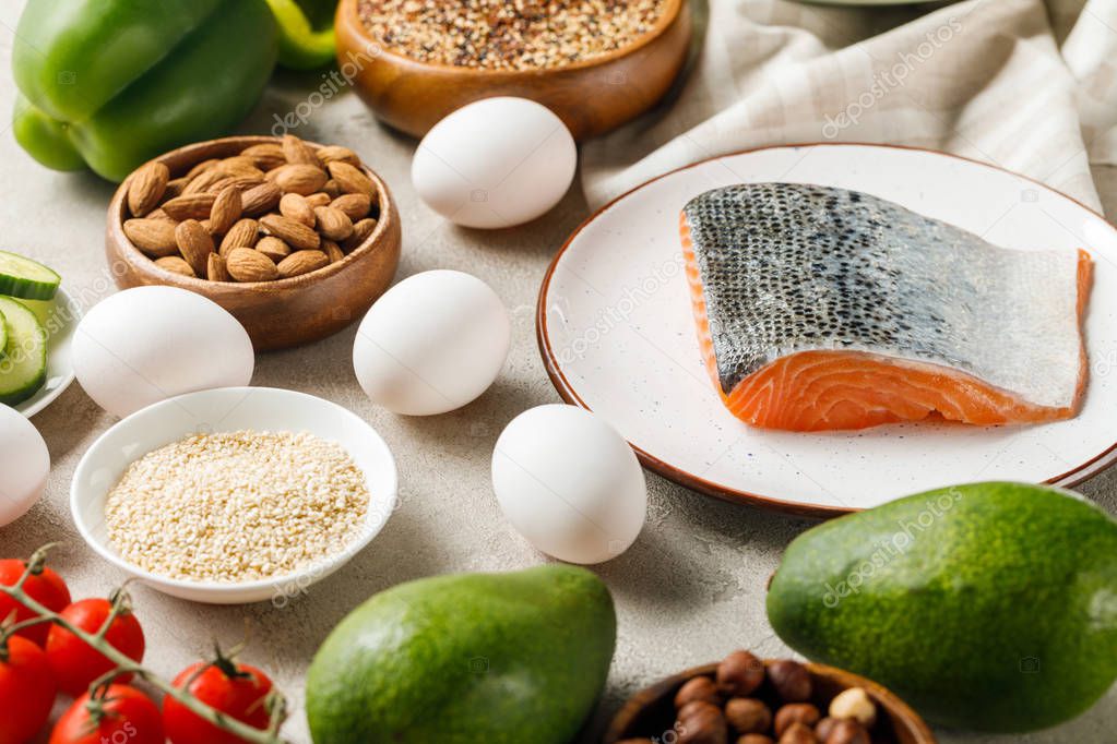 raw salmon on white plate near nuts, vegetables and eggs, ketogenic diet menu