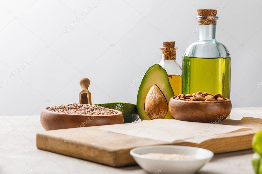 nuts and avocado on wooden chopping board near oil and groats isolated on grey, ketogenic diet menu