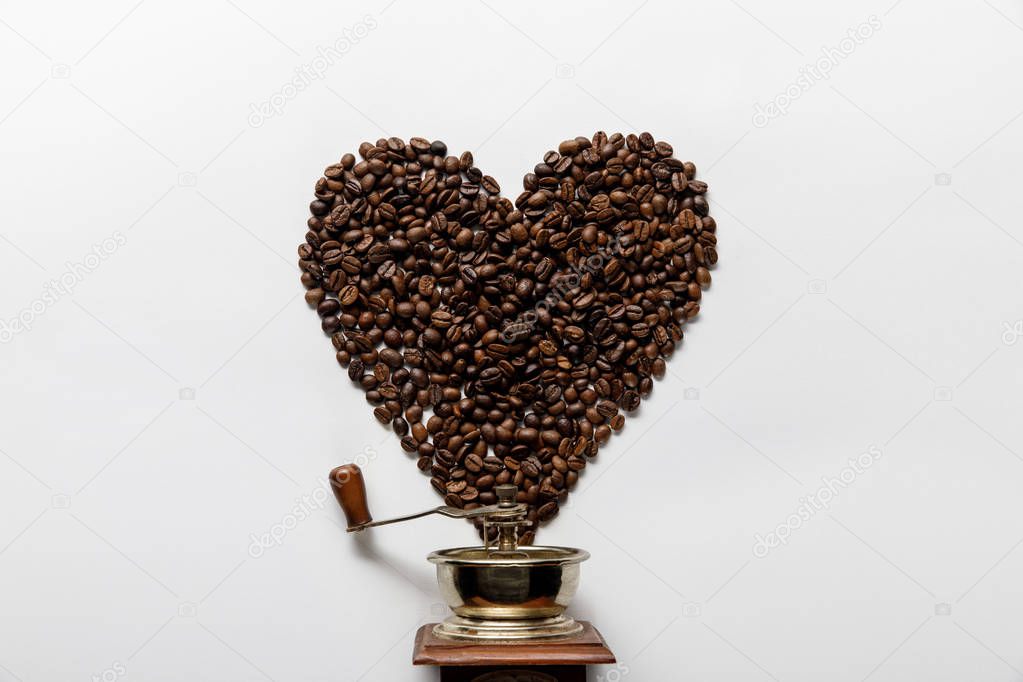 top view of heart made of coffee grains near vintage coffee grinder on white background