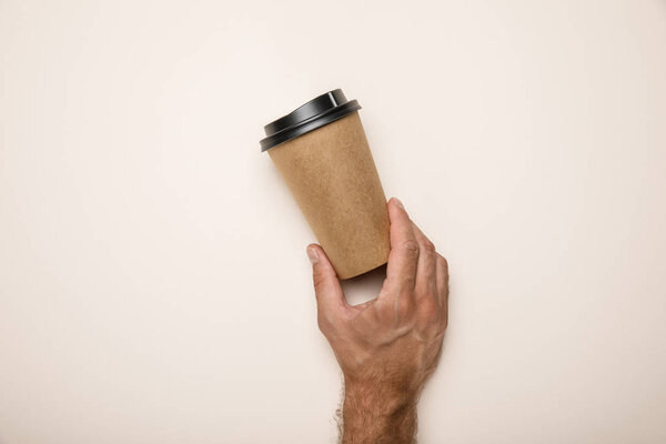 cropped view of man holding paper cup on beige background
