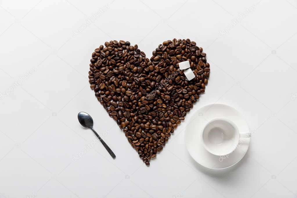 top view of empty cup near heart made of coffee grains with sugar on white background