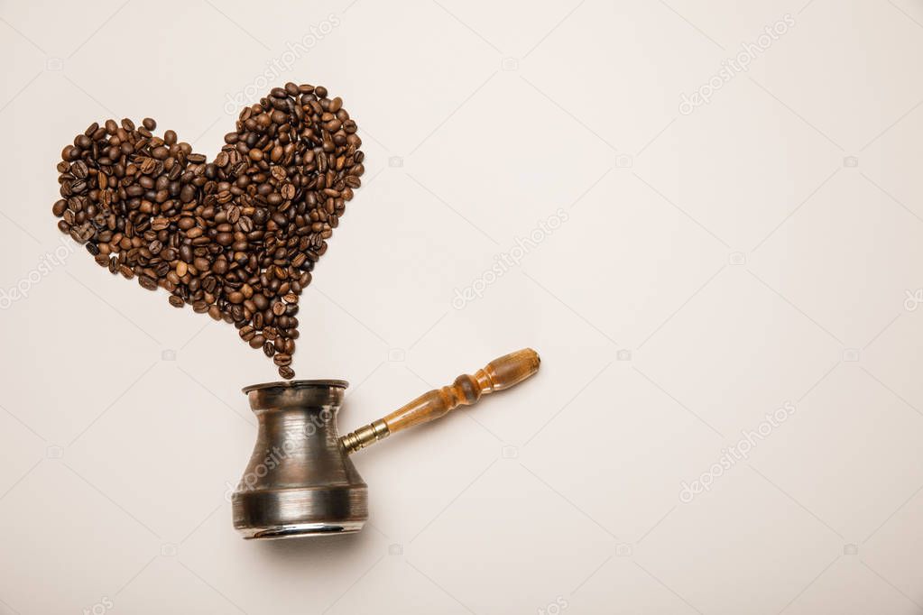 top view of heart made of coffee grains and cezve on beige background