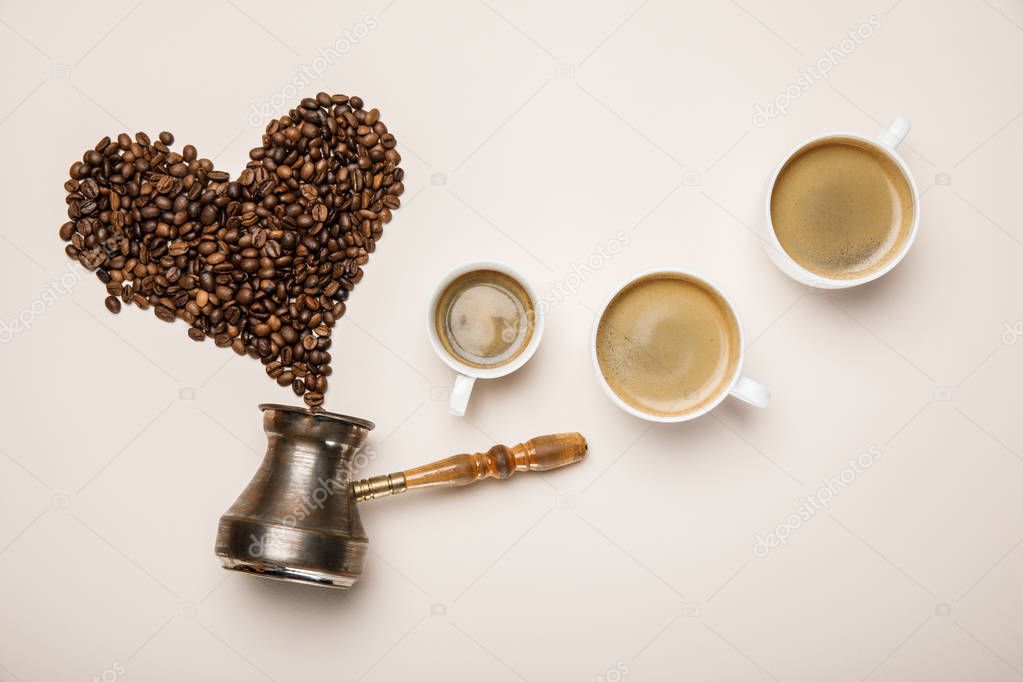top view of cups with fresh coffee near heart made of coffee grains and cezve on beige background