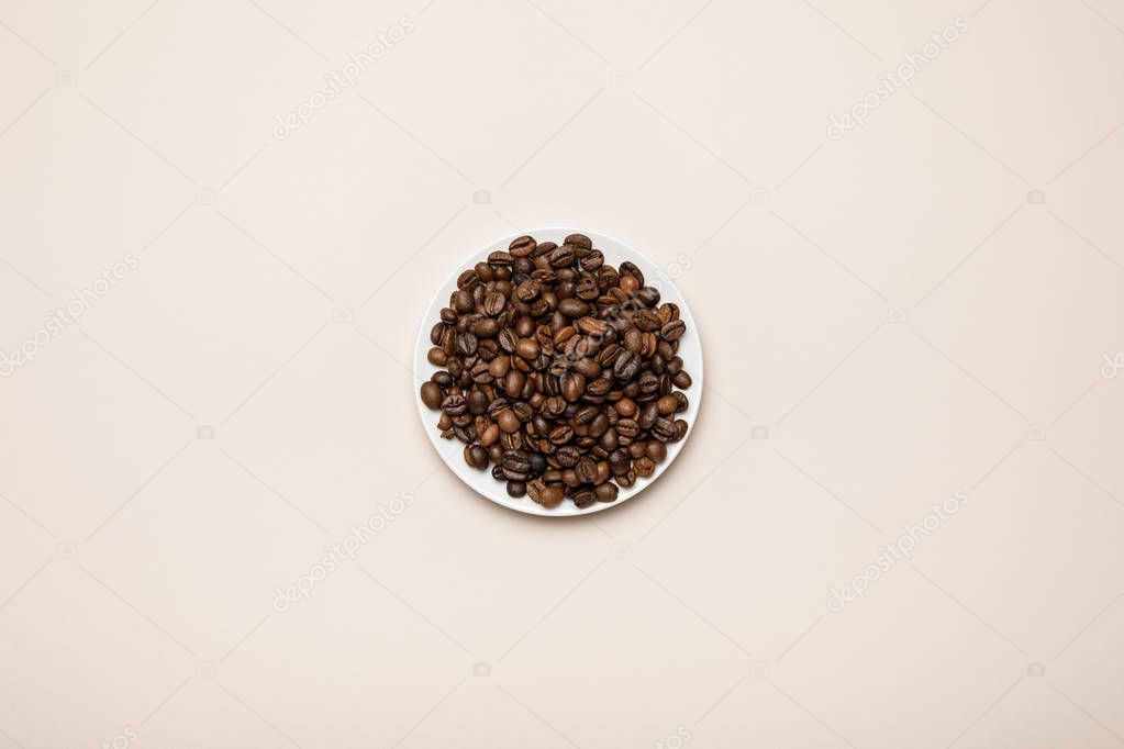 top view of coffee grains on white saucer on beige background