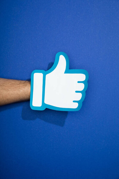 cropped view of man holding white paper thumb up on blue