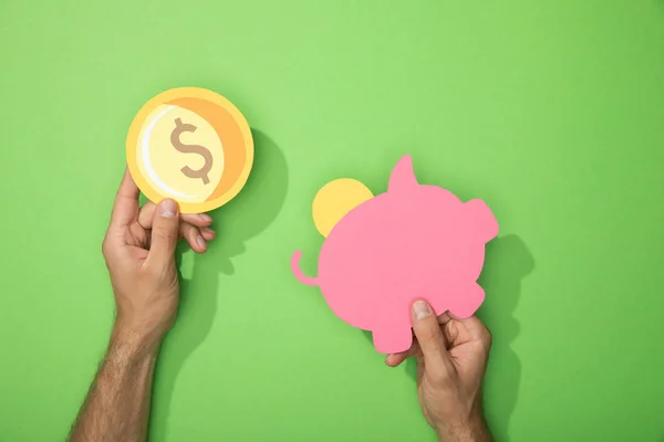 裁剪视图的人拿着纸小猪银行和硬币的绿色 — 图库照片