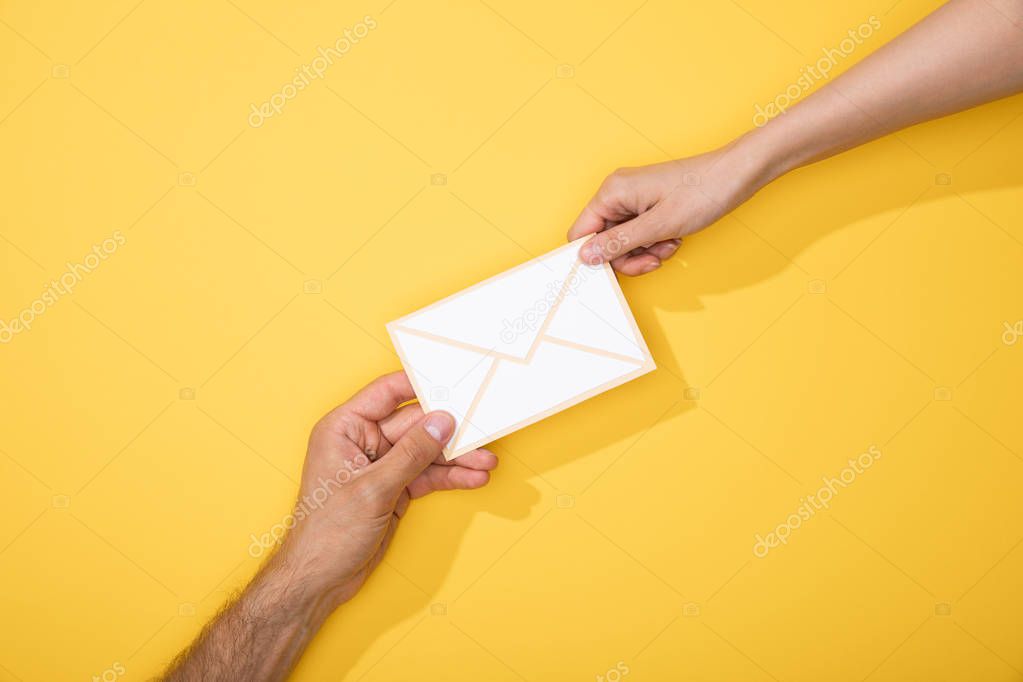 Cropped view of man and woman holding paper icon of white envelope on yellow