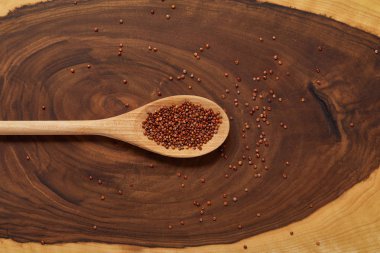top view of red quinoa in wooden spoon on beige and brown table clipart