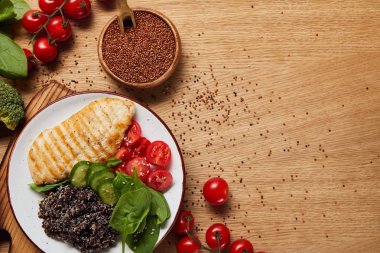 top view of cooked quinoa with grilled chicken breast and vegetables on white plate near raw red quinoa  seeds in wooden bowl clipart