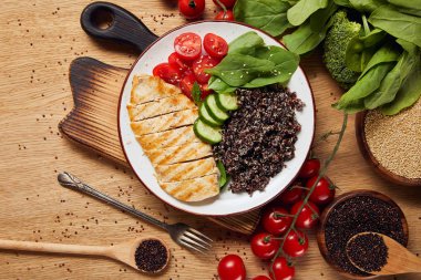 ahşap doğrama tahtası üzerinde beyaz plaka üzerinde ızgara tavuk göğsü ve sebze ile pişmiş Quinoa üst görünümü
