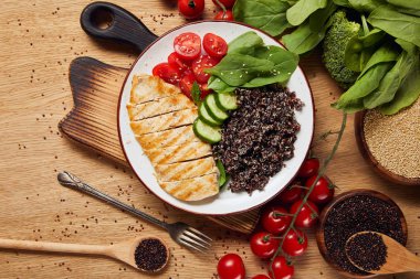 top view of cooked quinoa with grilled chicken breast and vegetables on white plate on wooden chopping board clipart