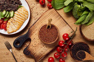 çiğ tohumlu doğrama tahtası yakınında beyaz plaka üzerinde ızgara tavuk göğsü ve sebze ile pişmiş Quinoa üst görünümü