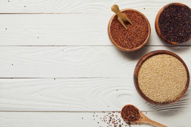 top view of white, black and red quinoa in wooden bowls on white table with copy space clipart