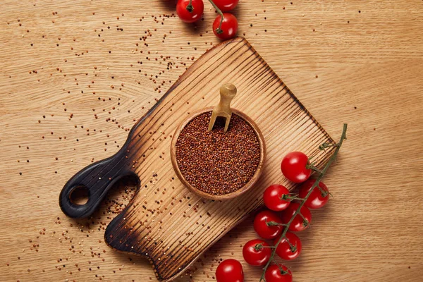 top view of red quinoa seeds in wooden bowl on chopping board near red tomatoes