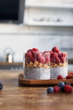 selective focus of yogurt with chia seeds, oat flakes and raspberries on wooden tray in kitchen clipart