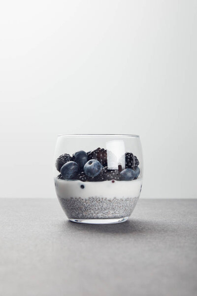 tasty yogurt with chia seeds, blueberries and blackberries on marble surface isolated on grey