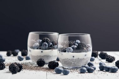 siyah üzerinde izole beyaz masa üzerinde dağınık tohum, yaban mersini ve böğürtlen yakın gözlük Chia tohum ve çilek ile yoğurt seçici odak