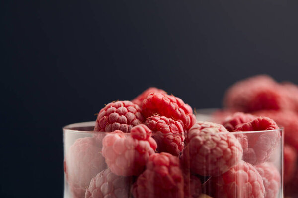 selective focus of fresh raspberries in glasses isolated on black