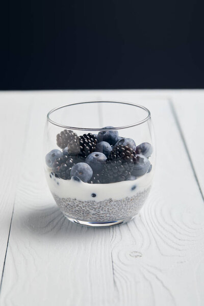 glass with blueberries, blackberries and yogurt with chia seeds on white wooden table isolated on black