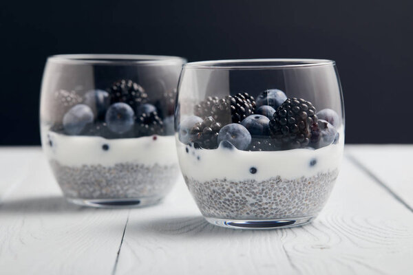 selective focus of yogurt with chia seeds, blueberries, blackberries on white wooden isolated on black