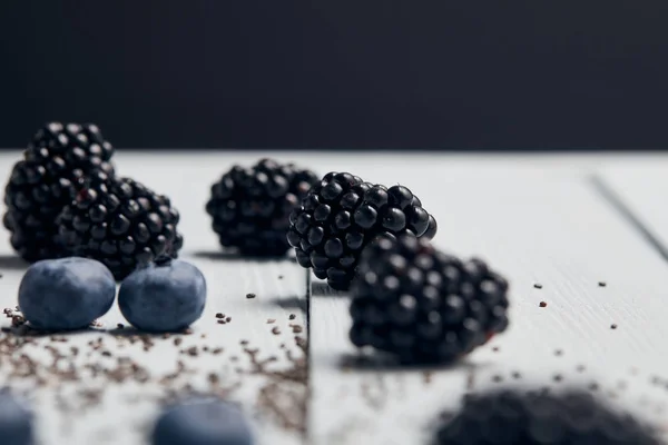 ブラックベリー ブルーベリー 黒で分離されたテーブルの上に散らばったチアシードの選択的な焦点 — ストック写真