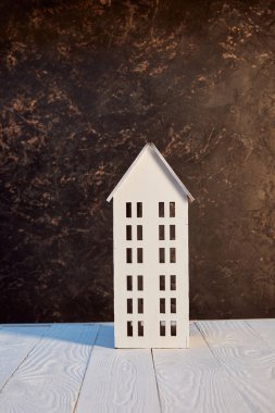 Beyaz ahşap masa üzerinde ev modeli kahverengi dokulu duvar, gayrimenkul kavramı yakın