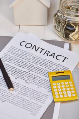 Sözleşme ve hesap makinesi, gayrimenkul kavramı ile beyaz ahşap masa üzerinde ev modeli